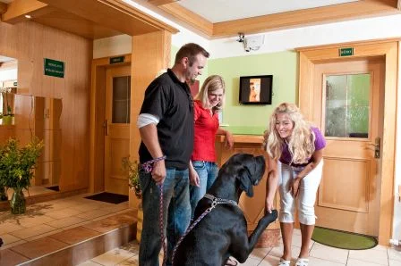 „Gerti Gruber begrüßt einen Hund mit Gästen in der Lobby des GRUBERS Hotel-Apartments Gastein – persönlicher Empfang auf vier Pfoten