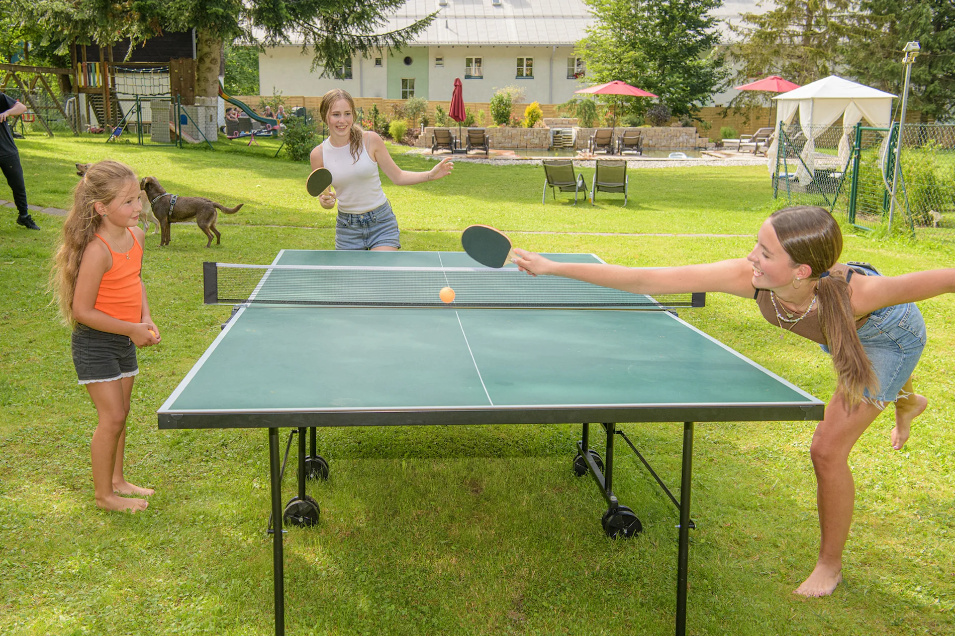 Sommerurlaub mit Hund in Gastein – Kinder spielen Tischtennis im Garten, Hund läuft im Hintergrund